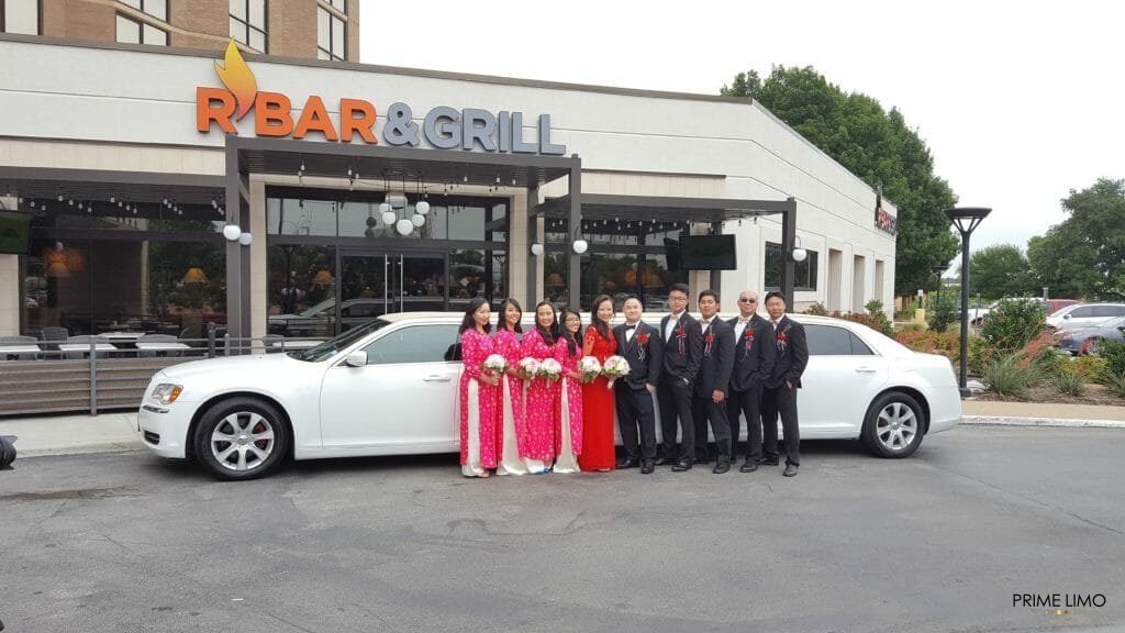 Bridal party outside of hotel restaurant  posing in front of white limo during the day
